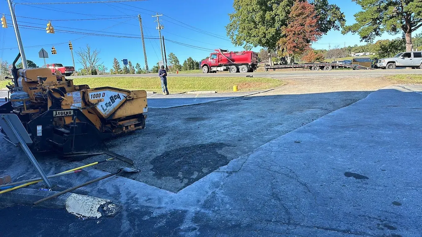 Asphalt paver beside a localized pavement repair
