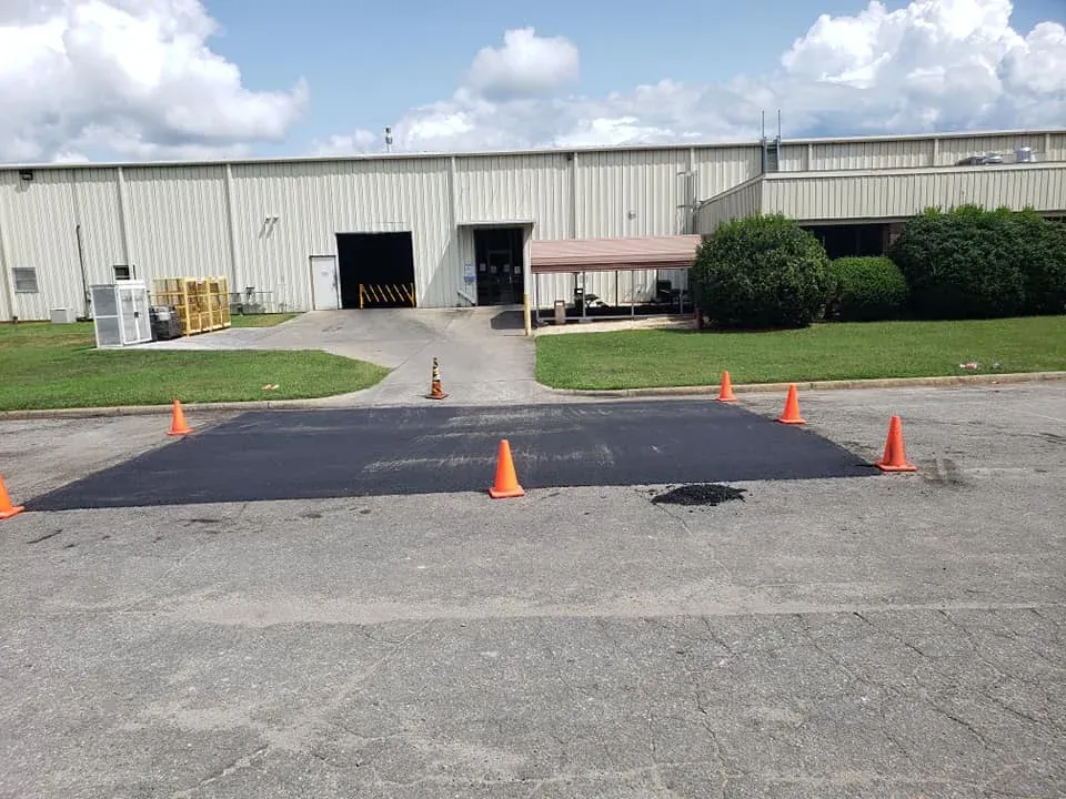 Fresh rectangular asphalt repair with safety cones outside a commercial building