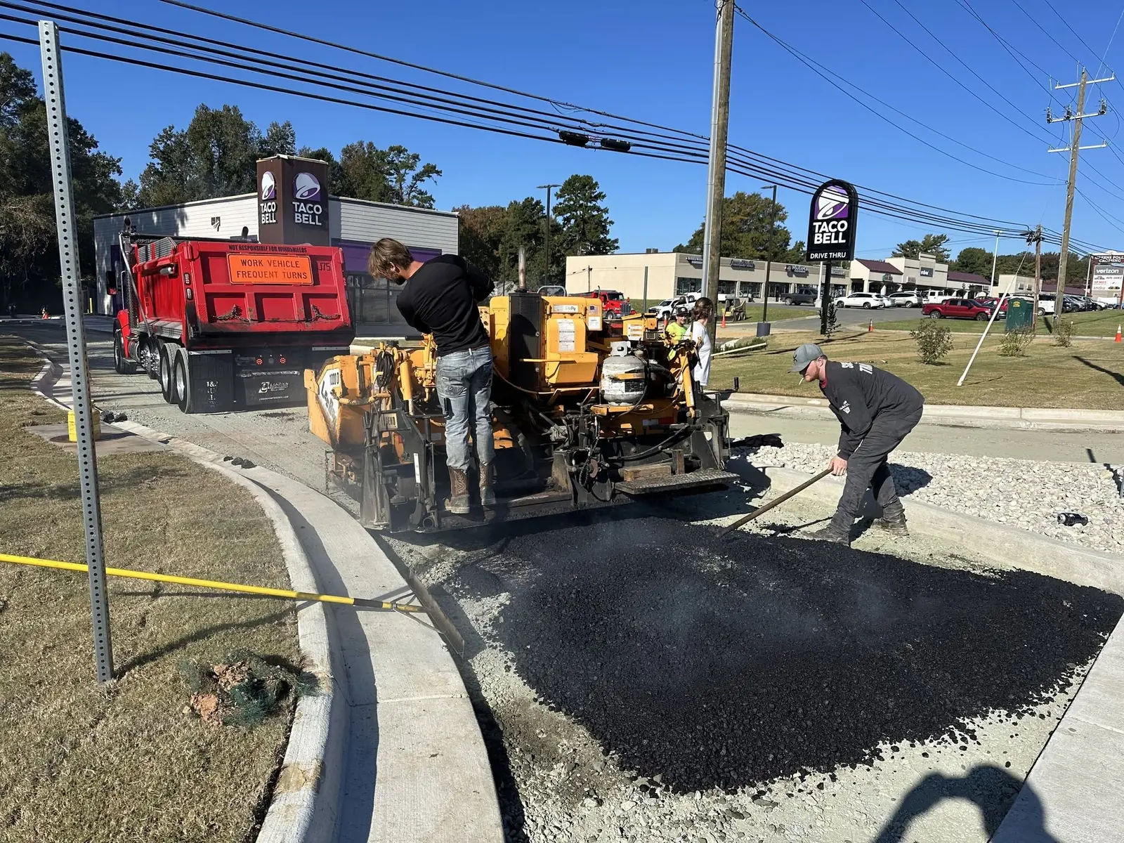 Asphalt paving crew and red dump truck working beside a commercial curb