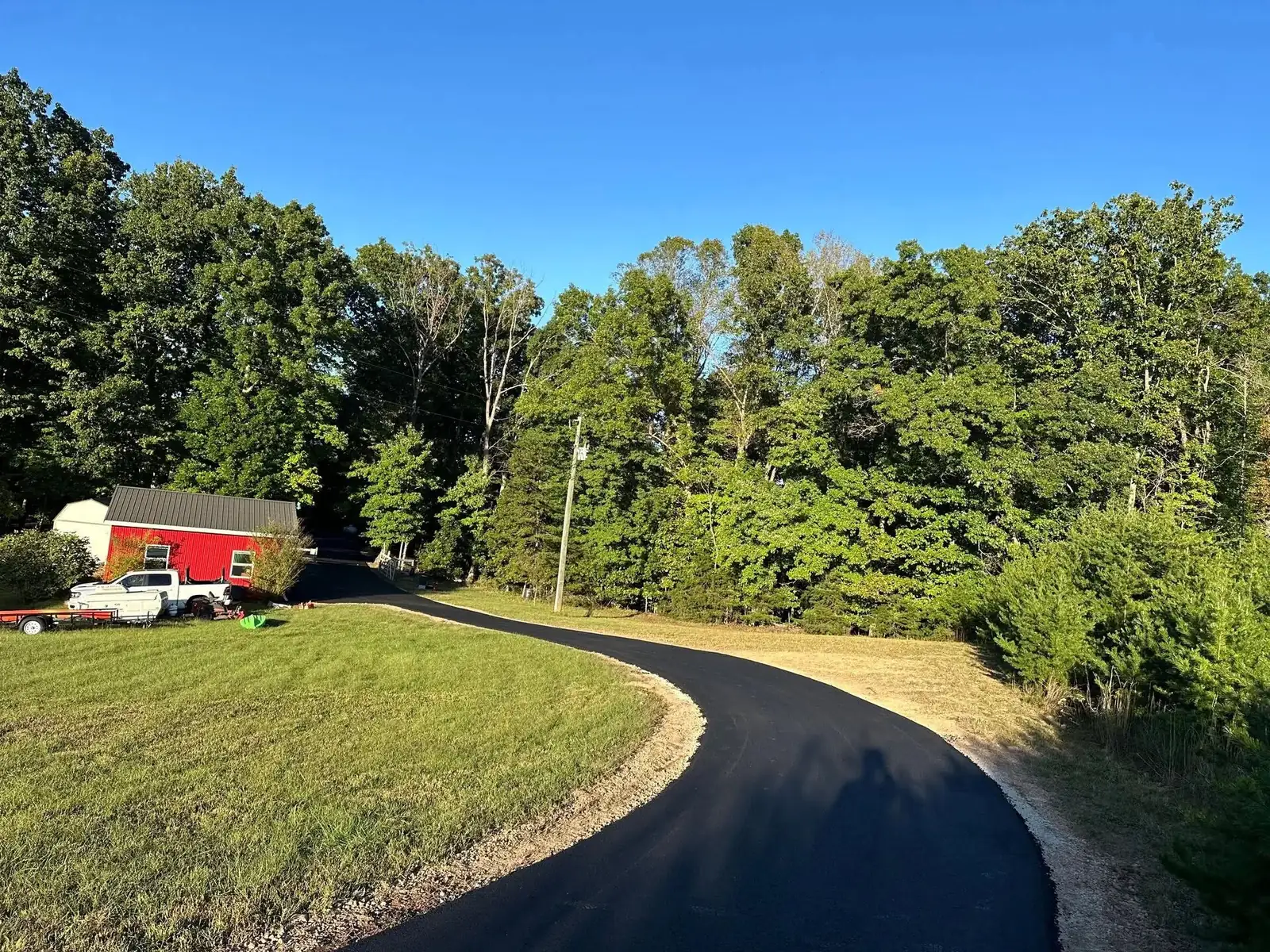 Smooth black asphalt driveway winding toward a red outbuilding