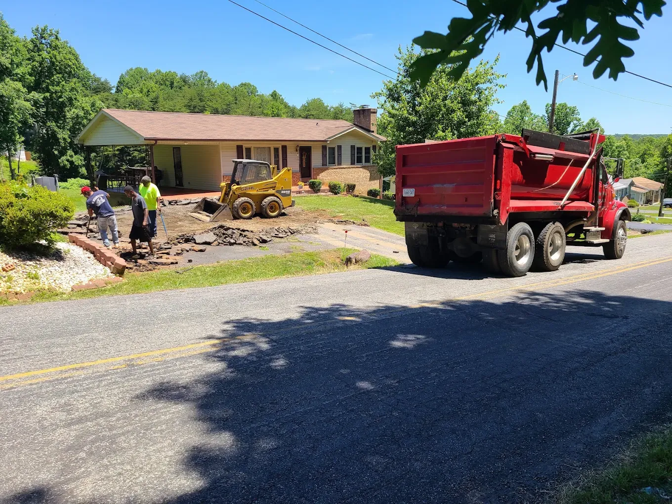 Crew removing broken driveway asphalt with a skid steer and red dump truck