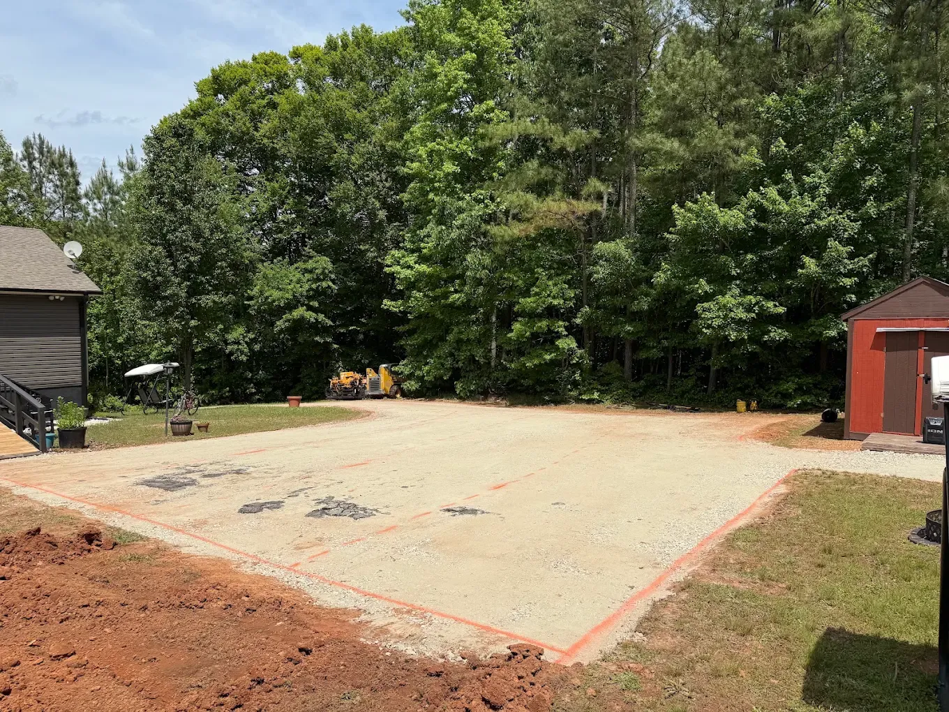 Prepared compacted base beside a red shed before asphalt placement