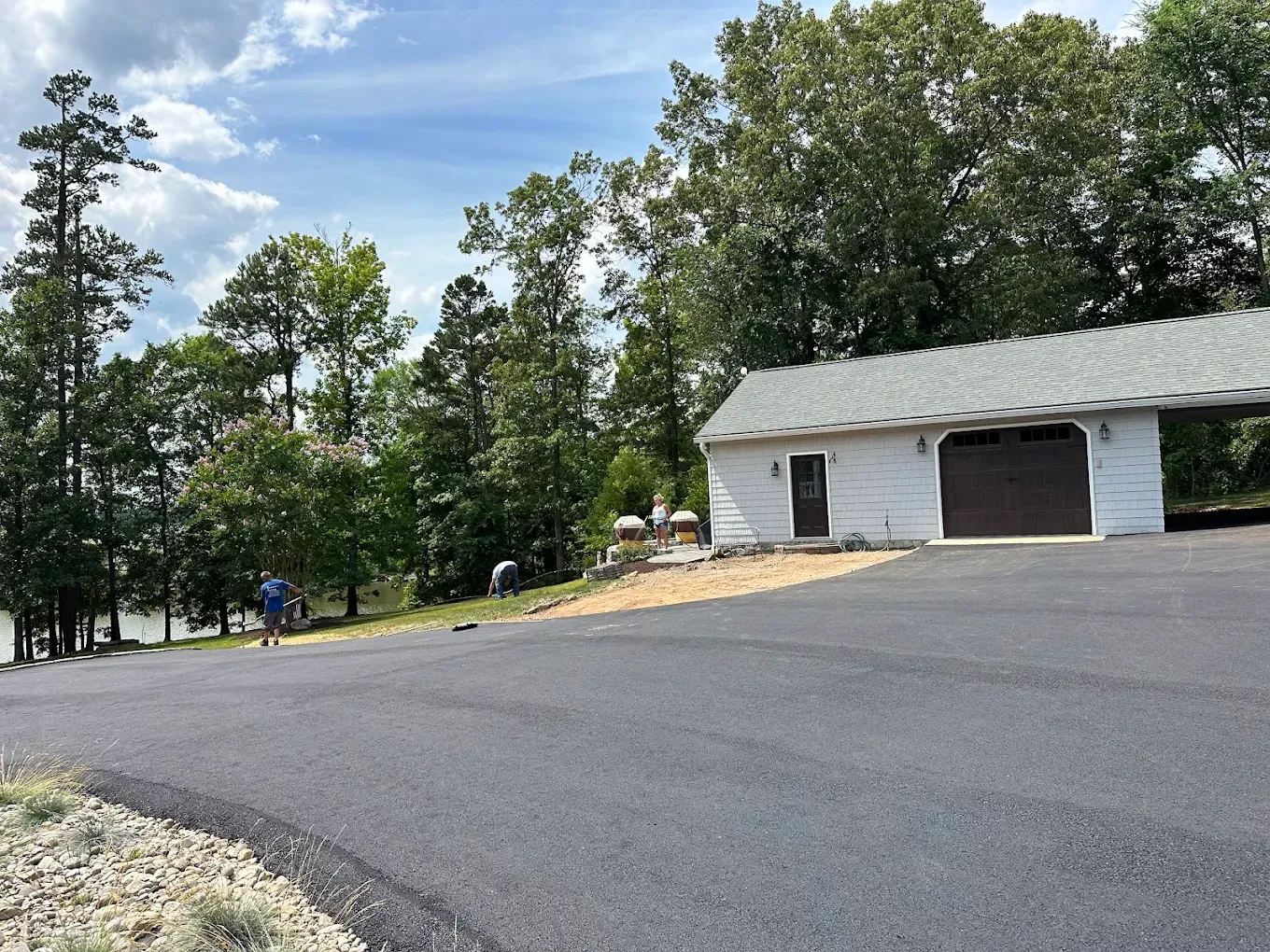Fresh asphalt driveway and parking apron beside a white garage