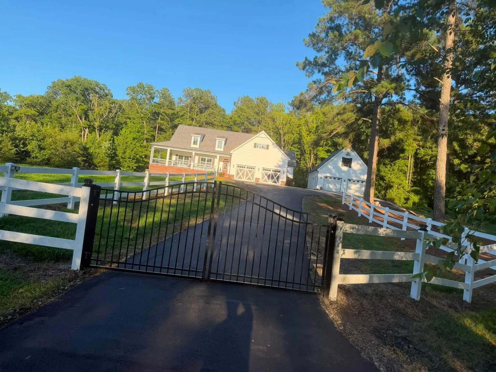 Paved residential entrance between white fences and a black gate