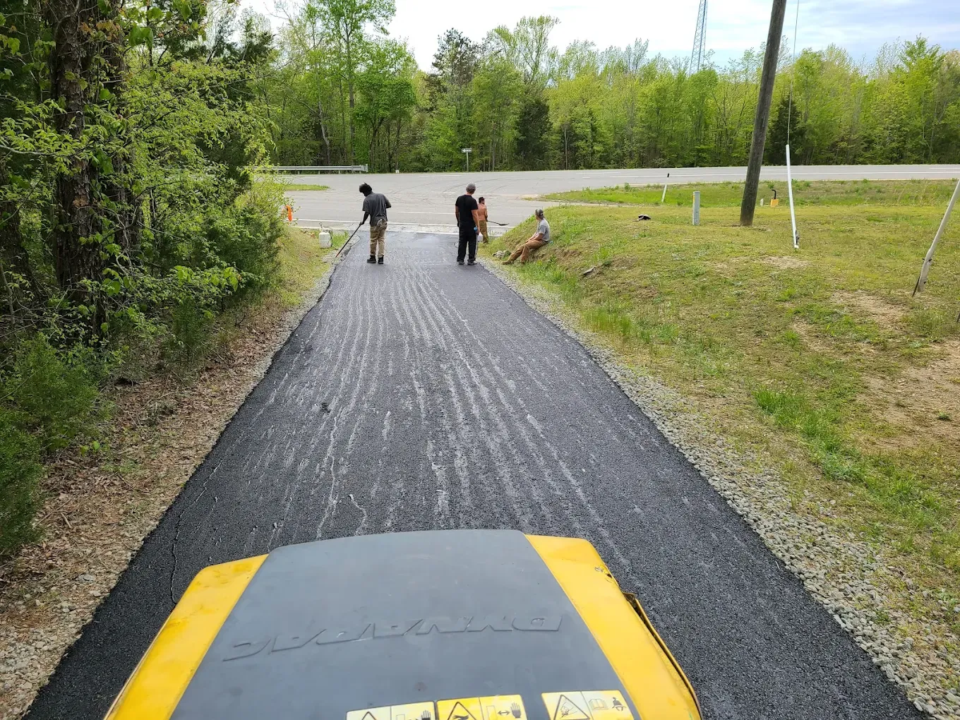 Crew finishing a narrow asphalt lane with a roller in the foreground
