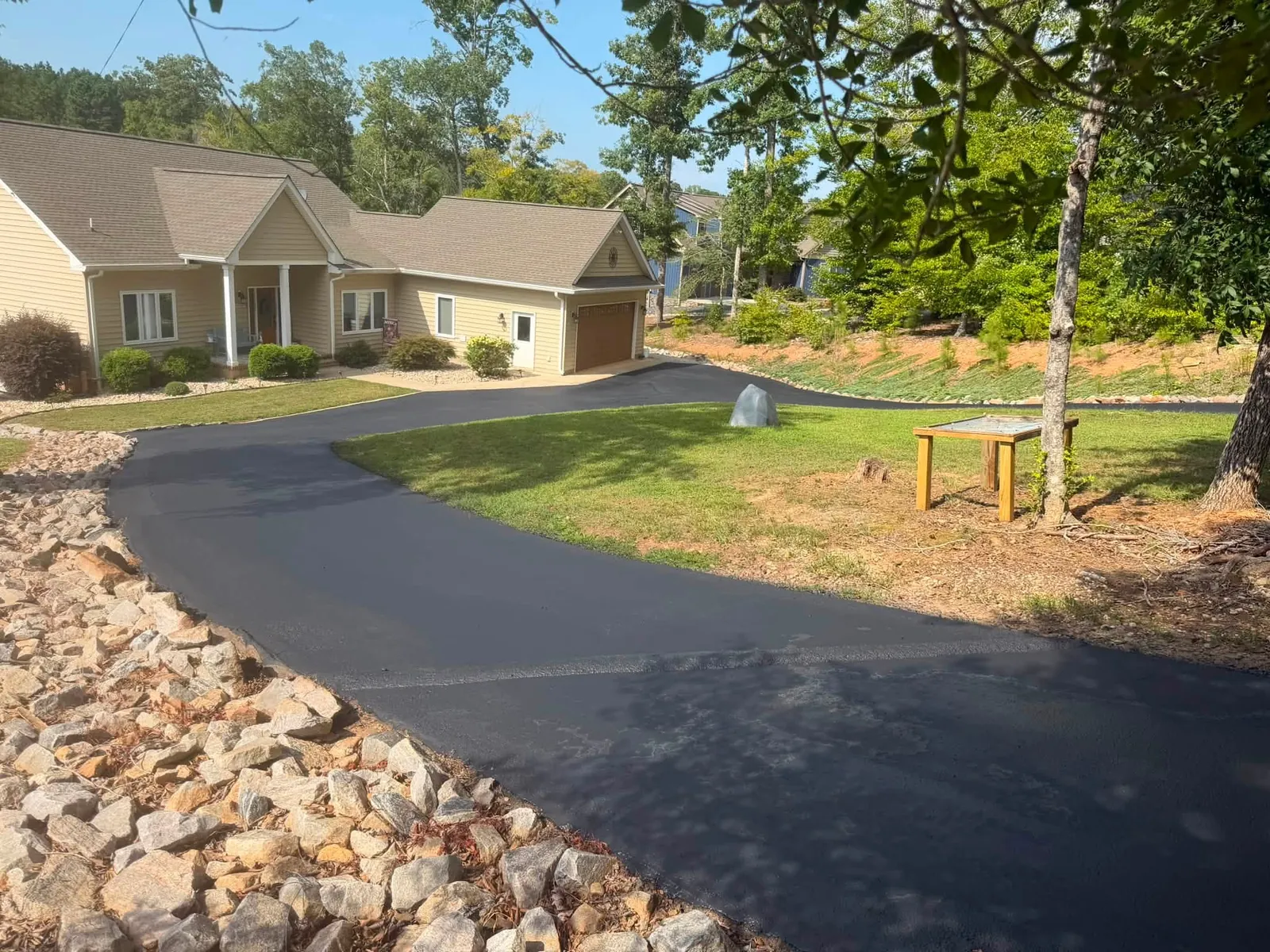 Curving asphalt driveway bordered by decorative stone and lawn