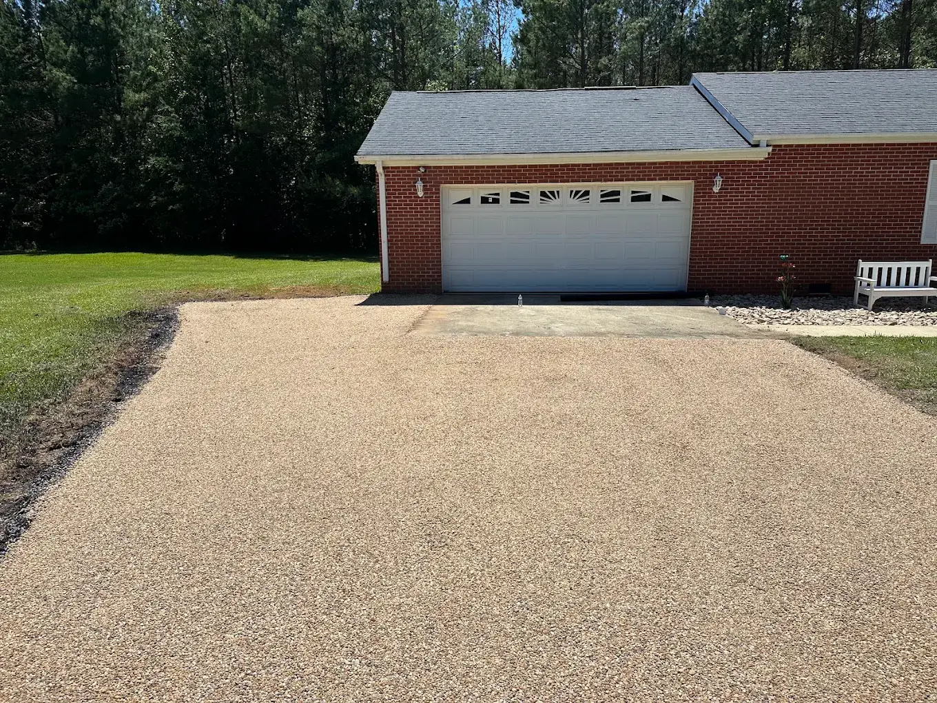 Tan stone-textured driveway leading to a white garage door at a brick home