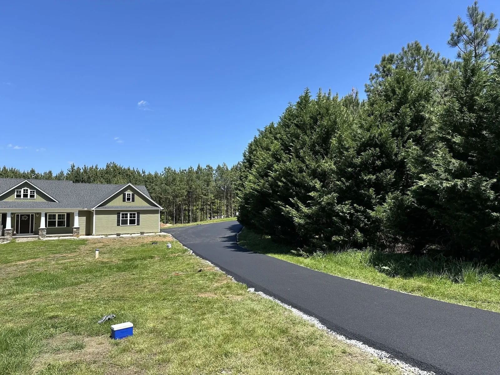 Fresh asphalt driveway curving past a landscaped lawn and home